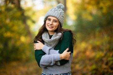 Young beautiful girl smiles laughing outdoors in hat and scarf gray cardigan sunset sun in autumn park