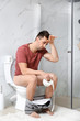 © New Africa - Man with paper roll sitting on toilet bowl in bathroom