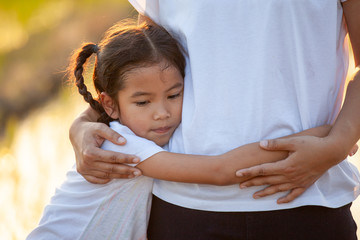 Sad asian child girl hugging her mother  in the paddy field with the sunlight