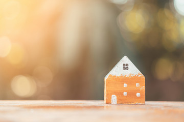 Wall Mural - Small home model on wooden table with nature green bokeh abstract background. Family life and business real estate concept.