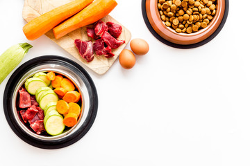 Wall Mural - Pet feed ingredients. Raw meat and fresh vegetables near bowl with dry feed on white background top-down copy space