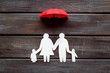 Health insurance concept. Family cutout under umbrella on dark wooden background top-down copy space