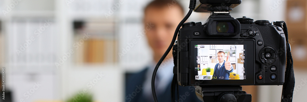 Male in suit and tie show confirm sign arm making promo videoblog or photo session in office camcorder to tripod closeup. Vlogger promotion selfie solution or finance advisor management information - obrazy, fototapety, plakaty 