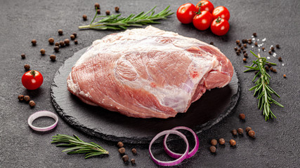 Wall Mural - A large piece meat of raw pork, hip or tenderloin on a black background with vegetables and spices, background image, copy space text