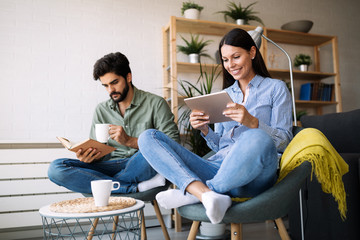 Young couple reading together book and ebook, sitting on couch