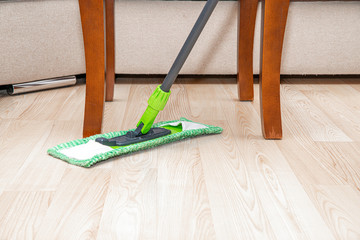 Wall Mural - Cleaning the floor with a mop. The concept of care for the cleanliness of the apartment. The man wipes the floor with a green mop. A man cleaning the apartment.