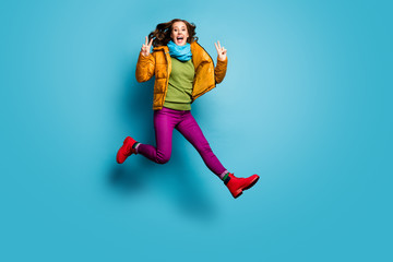 Full length photo of pretty lady jump high up showing v-sign symbols wear casual yellow overcoat scarf violet pants red boots green pullover isolated blue color background