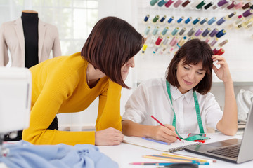 Two young female dressmakers working in sewing studio. Sisters start family business. Bespoke tailoring. Private enterprise. Hobby and business