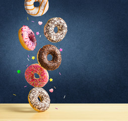 Wall Mural - Flying donuts. Mix of multicolored sweet doughnuts with sprinkel falling on the table on dark blue textured background.