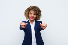 Young Woman African American Feeling Happy And Confident, Pointing To Camera With Both Hands And Laughing, Choosing You Against Flat Wall