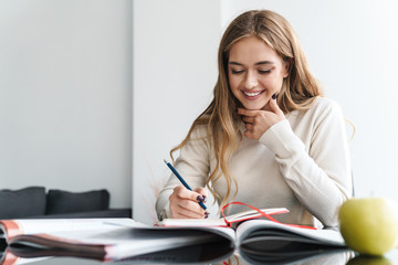 Wall Mural - Photo of young happy woman smiling and making notes in exercise book