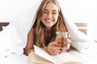 © Drobot Dean - Photo of young laughing woman reading book and drinking tea while lying