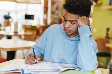 Wall Mural - Smiling african bot teenager studying while sitting at the hub