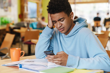 Sticker - Smiling african bot teenager studying while sitting at the hub