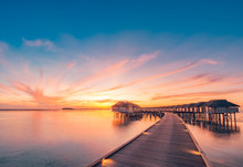Sunset On Maldives Island, Luxury Water Villas Resort And Wooden Pier. Beautiful Sky And Clouds And Beach Background For Summer Vacation Holiday And Travel Concept