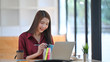 © Prathankarnpap - photo of young beautiful designer in red shirt taking notes in front of her laptop at the wooden desk over the modern office background.