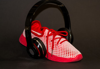 Wall Mural - On black background, red sneakers with large black headphones to listen to music when running. Sport. Street style and fashion. Advertizing of footwear.