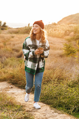 Sticker - Image of joyful young woman holding cellphone while walking outdoors