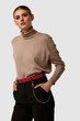A blonde lady in black trousers and beige high-neck top is posing on the gray background. A red leather belt is decorated with a steel buckle, metal eyelets and steel chain with a lobster clasp.