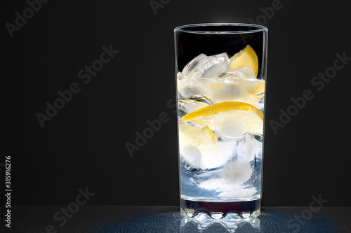 Cuadros en Lienzo glass cup with water, ice cubes and lemon on a dark background