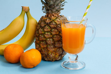 Fresh tropical fruits and glass of juice on blue background.