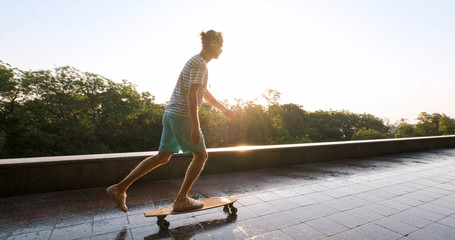 Handsome young male with skateboard outdoors in the city listen to music with headphones	