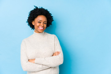 Wall Mural - Middle aged african american woman against a blue background isolated smiling confident with crossed arms.