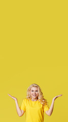 Wall Mural - Young happy woman shows hands up, spreads his hands to the sides. Above is an empty place for text and inscription on a yellow background. vertical shot