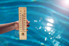 Woman Holding Thermometer On The Pool Background. Hot Weather And Summer Concept