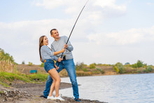 Happy Young Couple Fishing By Lakeside A