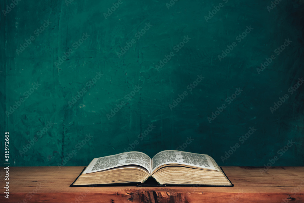 Open bible on a red old wooden table. Beautiful green wall background. - obrazy, fototapety, plakaty 