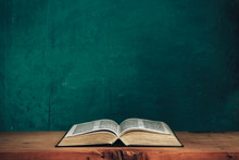 Open Bible On A Red Old Wooden Table. Beautiful Green Wall Background.