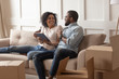 © fizkes - Smiling black family couple sitting on couch with tablet.