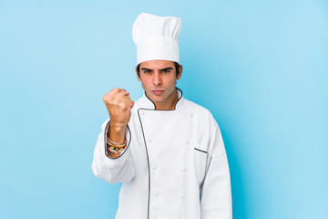 Wall Mural - Young cook man isolated showing fist to camera, aggressive facial expression.