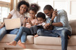 © fizkes - Happy addicted to gadgets black family using different devices.