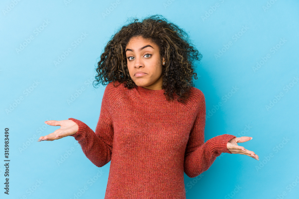 Young african american curly hair woman doubting and shrugging shoulders in questioning gesture. - obrazy, fototapety, plakaty 