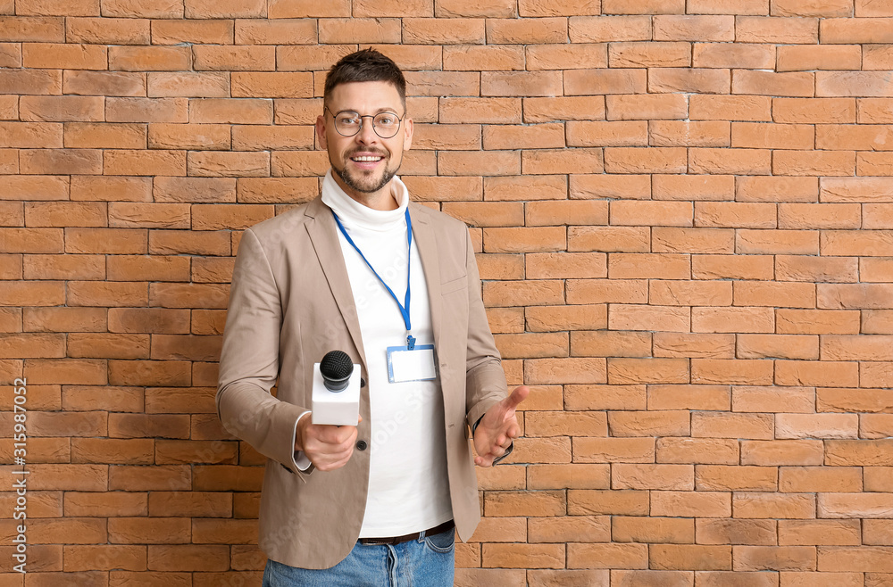 Male journalist with microphone on brick background