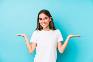 Young caucasian woman  isolated makes scale with arms, feels happy and confident.