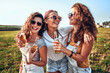 Leinwandbild Motiv Candid of young attractive three girl group of friends cheers holding a bottle beer drinking for celebration party in evening sunset