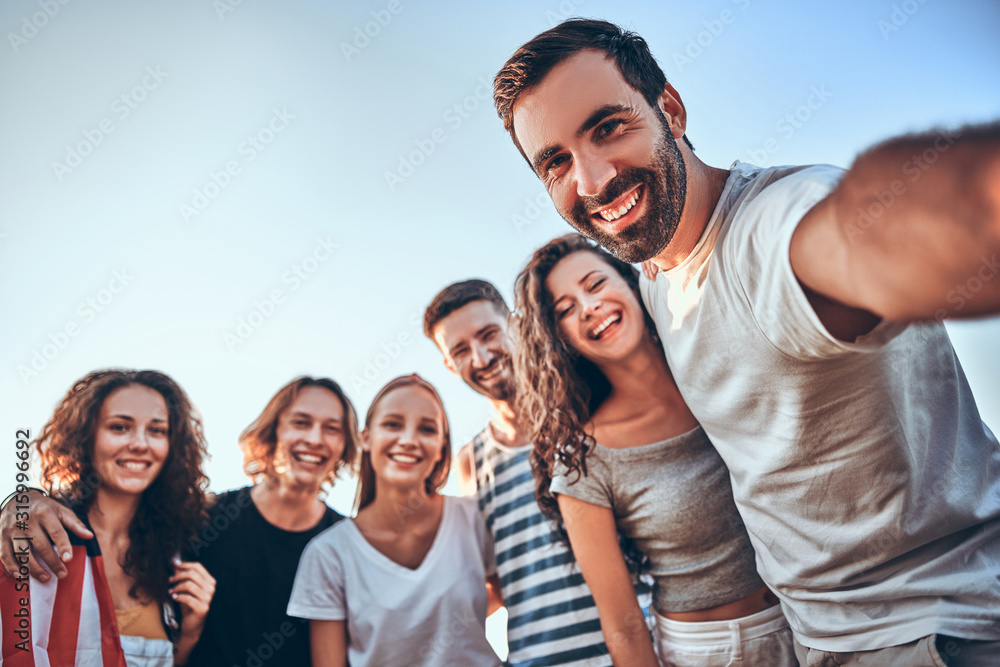 Group of happy teenage friends taking selfie on nature. Young woman with american flag background. - obrazy, fototapety, plakaty 