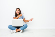 Young Mixed Race Indian Woman Sitting Working On Laptop Excited Pointing With Forefingers Away.