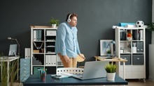 Slow Motion Of Funny Employee Attractive Guy Dancing In Office Room Wearing Headphones Having Fun Alone. Modern Gadgets, Joy And Entertainment Concept.