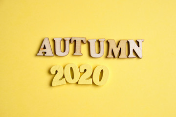 The concept of autumn in the new year. Wooden numbers 2020 with letters on a yellow background. Top view.