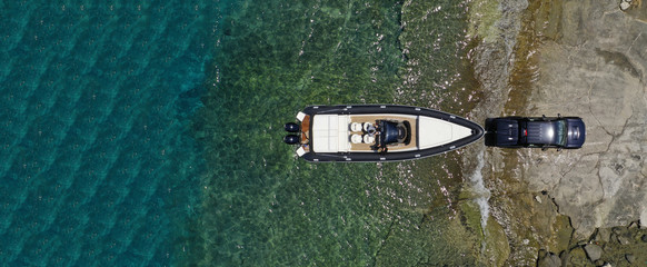 Aerial top view ultra wide photo of inflatable speed boat on trailer being towed by truck from emerald exotic sea to land