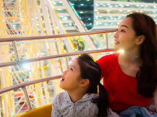 Wall Mural - happy asia mother and daughter have fun in amusement carnival park with farris wheel and carousel background