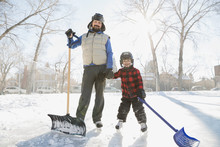 Portrait Of Father And Son With Snow Shovels On Ice Rink
