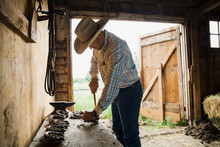 Rancher Cleaning Horseshoe At Workbench In Barn