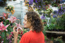 Woman Smelling Pink Lily In Plant Nursery Greenhouse