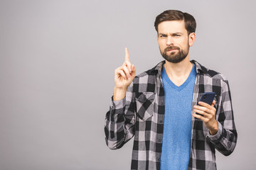 Idea! Young stylish hipster guy dressed in shirt, holds smart phone, reads something attentively, raises index finger, quotes someone words, proves his rightness. People and technology concept.