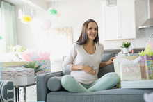Pregnant Woman With Baby Shower Gifts Sitting On Sofa